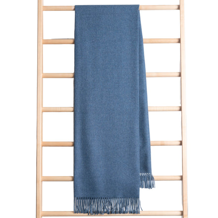 Blue throw with fringe draped over a wooden ladder on a white background