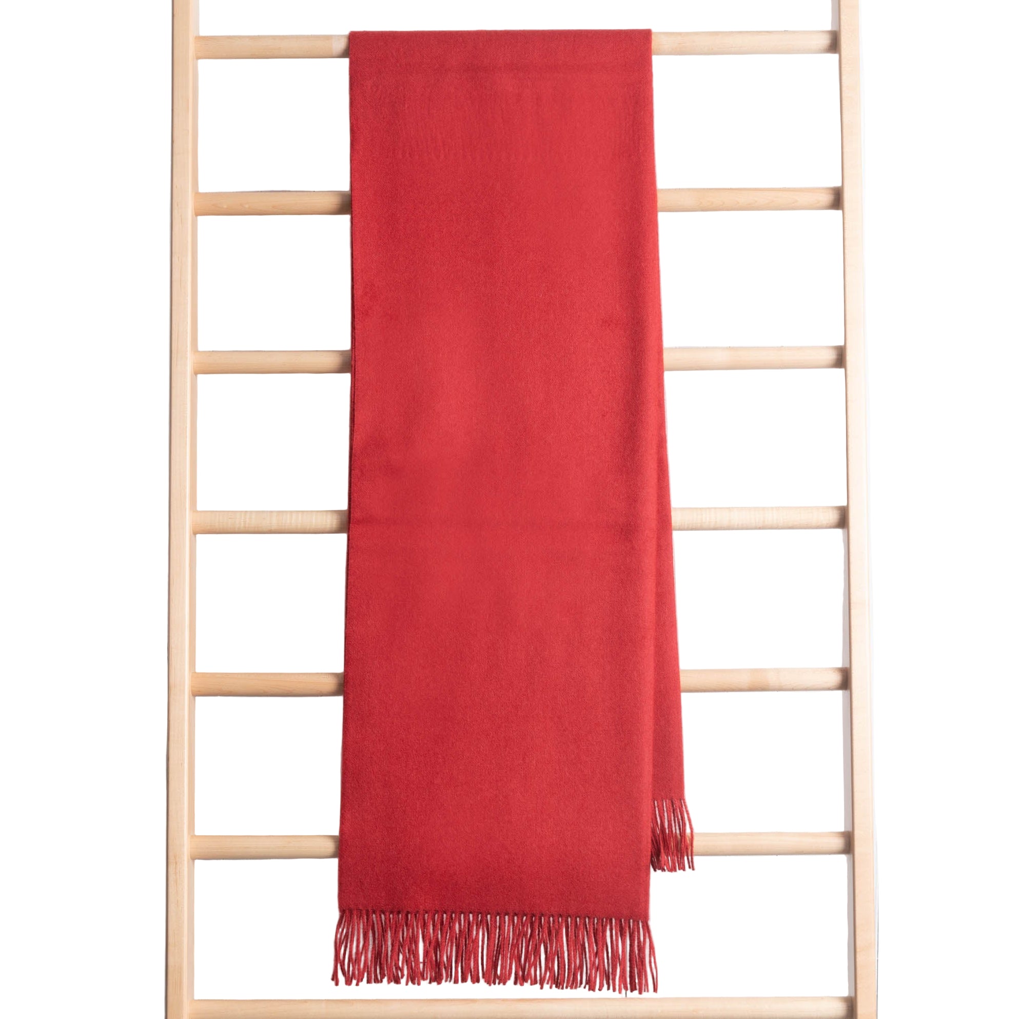 Red throw with fringes draped over a wooden ladder on a white background