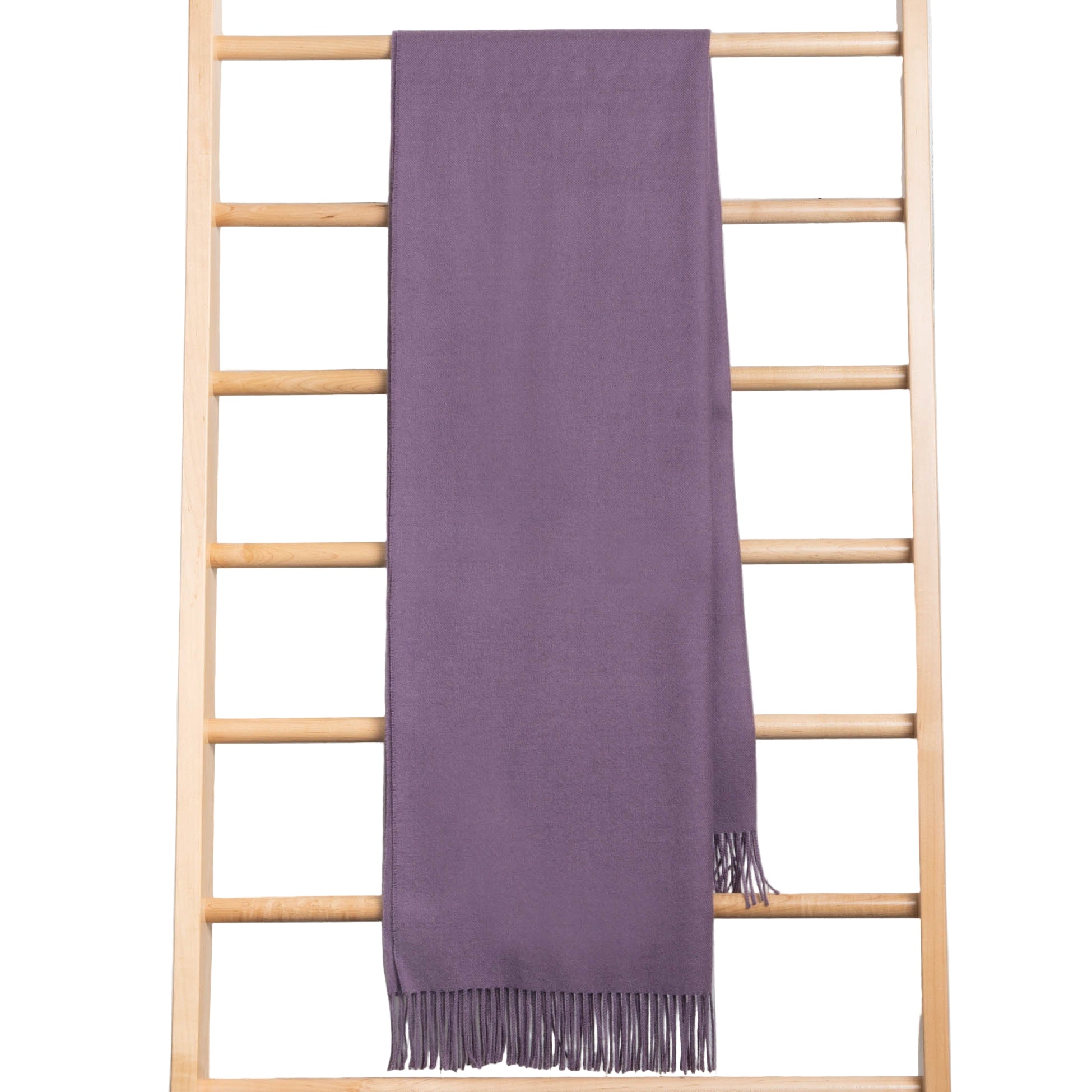 Purple throw with fringe draped over a wooden ladder against a light wooden panel background