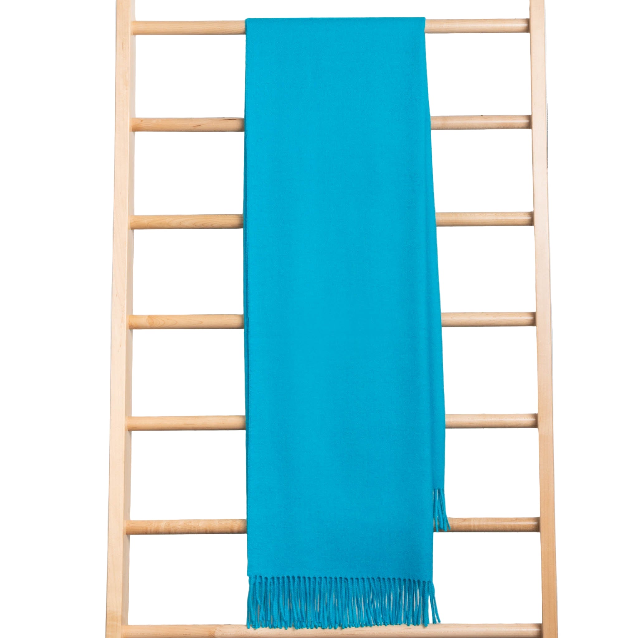 Turquoise throw with fringe draped over a wooden ladder against a light wooden panel background