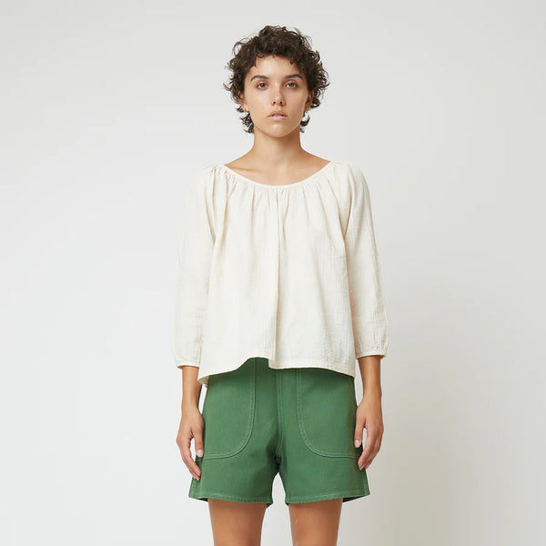 Atelier Delphine Afton Top in Crinkled Cotton, model wearing a white top and green shorts in front of a white background