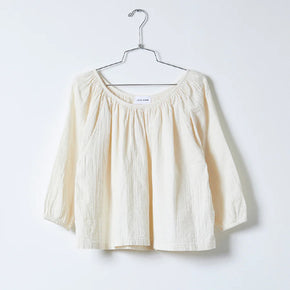 Atelier Delphine Afton Top in Crinkled Cotton, a white crinkled top hanging on a hanger on a white background
