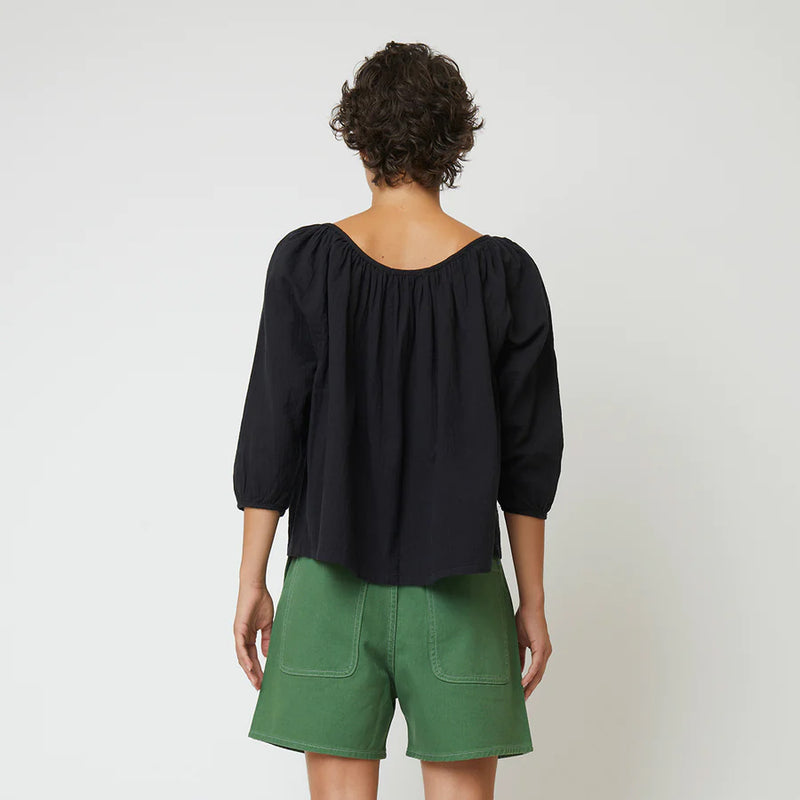 Atelier Delphine Afton Top in Crinkled Cotton, a woman facing away from camera wearing a black top and green shorts in front of white background