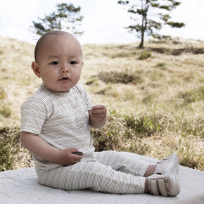 Serendipity Baby Jersey Pocket Suit - 100% GOTS cotton, a baby in a striped rainbow onesie sitting on a rock in a field