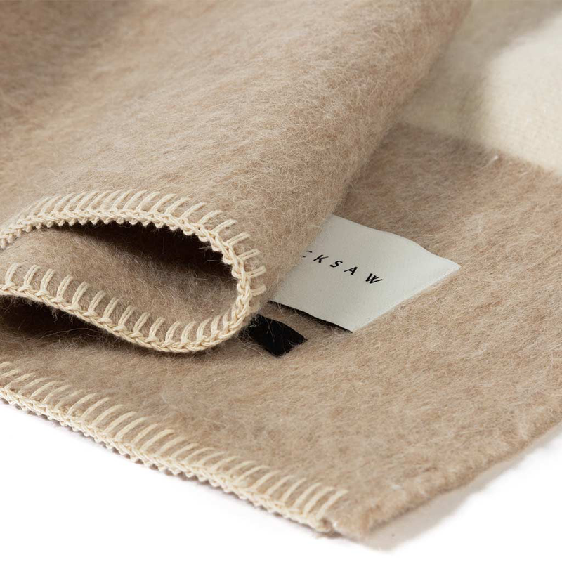 Blacksaw Siempre Recycled Blanket - Beige with Ivory Stripe, a closeup of the hem of a beige blanket with white stripe on a white background