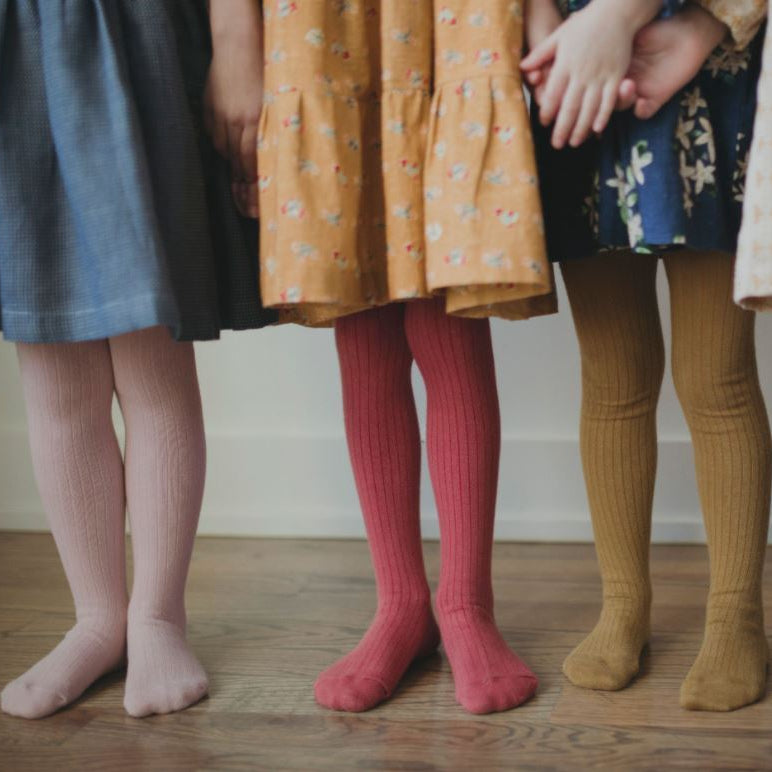 Children wearing colorful dresses and tights on a wooden floor.