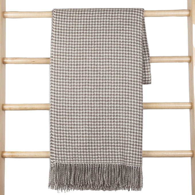 A beige and brown houndstooth patterned baby alpaca throw blanket with tassels displayed on a wooden ladder.