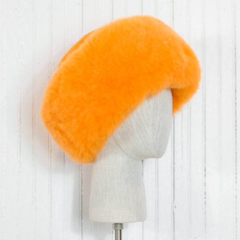 Premium Baby Alpaca Fur Hat. An orange Premium Baby Alpaca Fur Hat on a mannequin head against a white paneled background.