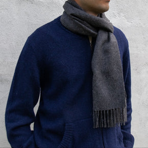 Man wearing a blue sweater and gray scarf against a gray concrete wall