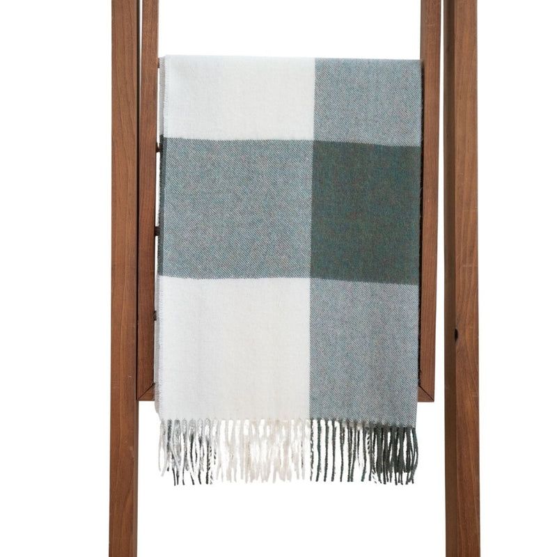 A baby alpaca shawl with a buffalo plaid pattern in gray and white colors, displayed on a wooden hanger.