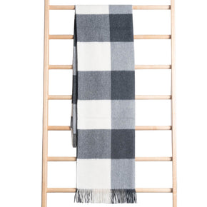A gray and white buffalo plaid baby alpaca throw blanket with tassels displayed on a wooden rack.