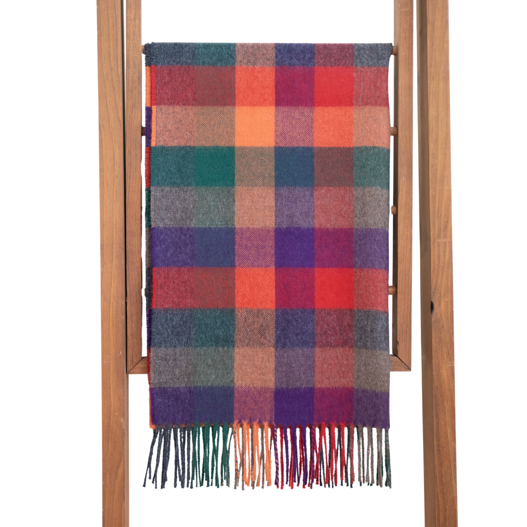A multicolored plaid baby alpaca shawl displayed on a wooden hanger, with a variety of colors including blue, red, orange, and purple.