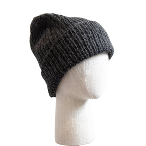 An oversized, gray knit alpaca hat displayed on a mannequin head against a white background with wooden panels.