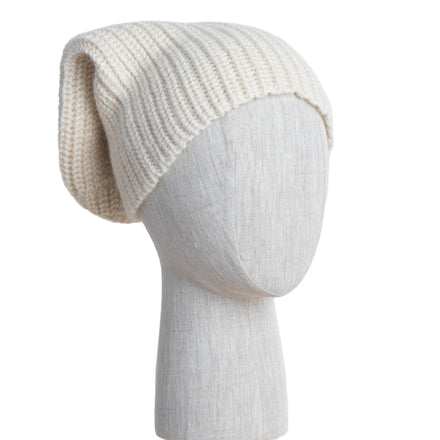 Knitted cream beanie on a mannequin head against a white wooden panel background