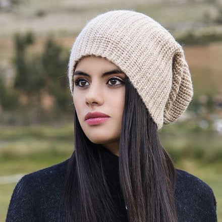 Woman wearing a beige knit beanie and dark coat.
