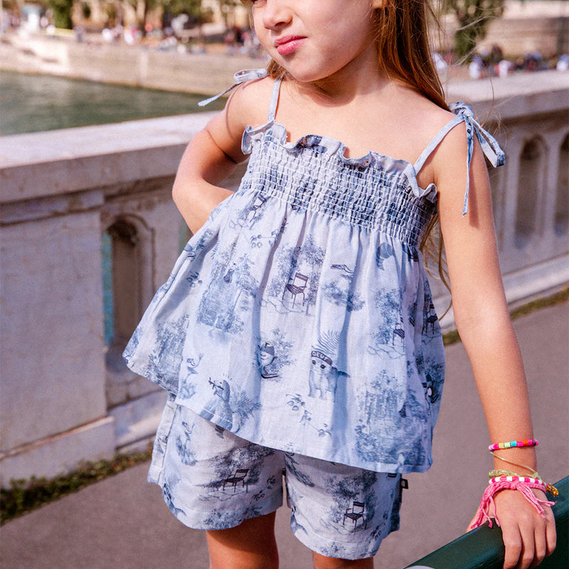 Oeuf Kids Smocked Set – 50% cotton, 50% linen blend for summer, a girl wearing a blue toile smock set in front of a bridge