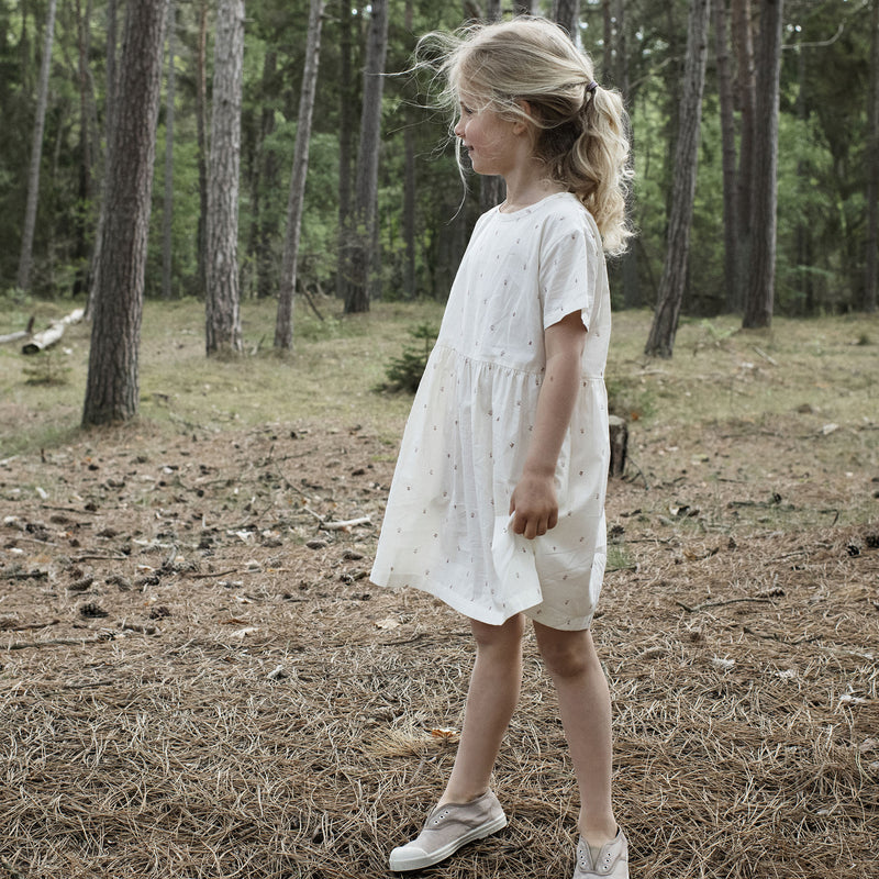 Serendipity Kid's Loose Dress - 100% Organic Cotton, a girl wearing a White dress with reddish-brownish flowers in a forest