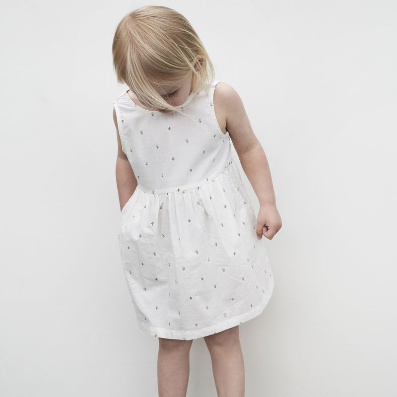Serendipity Kid's Peasant Dress - 100% Organic Cotton | Fluff Alpaca, a child looking down and wearing white peasant dress on a white background