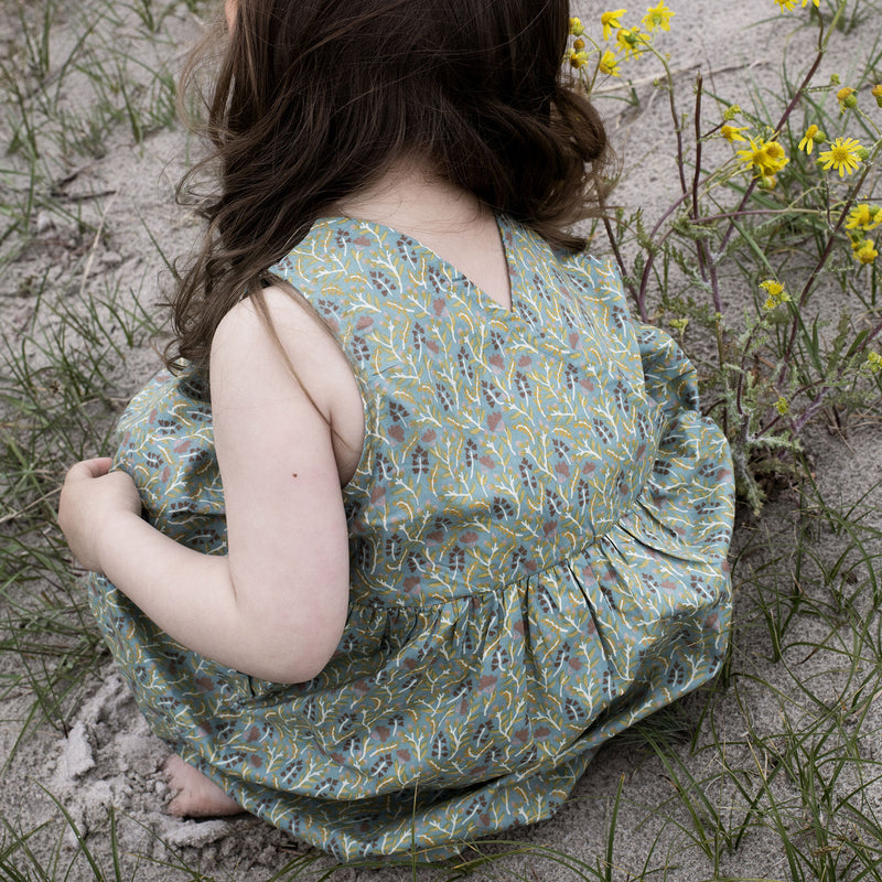 Serendipity Kid's Peasant Dress - 100% Organic Cotton | Fluff Alpaca, a child  bending down and facing away wearing a green peasant dress in field with yellow flowers