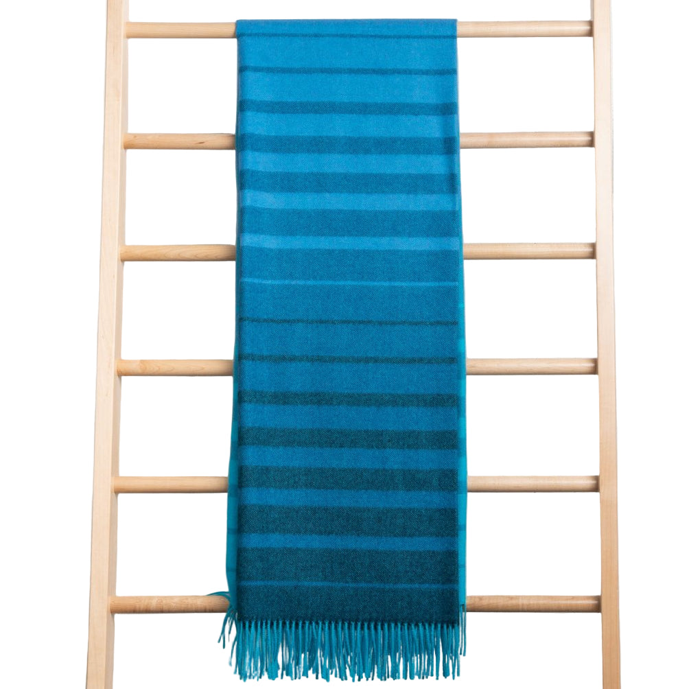 Blue striped throw with fringe on a wooden ladder against a white background
