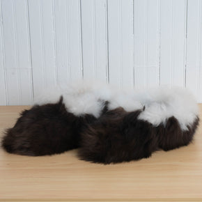 A pair of brown and white alpaca fur fuzzy slippers placed on a wooden surface against a white background.
