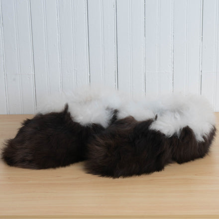 A pair of brown and white alpaca fur fuzzy slippers placed on a wooden surface against a white background.