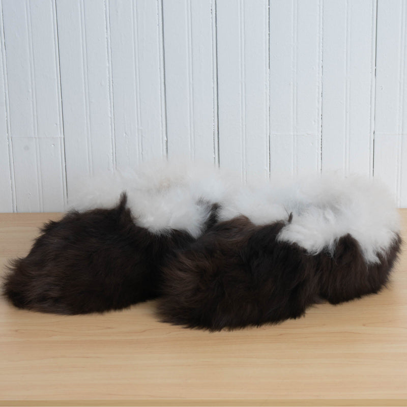 A pair of brown and white alpaca fur fuzzy slippers placed on a wooden surface against a white background.