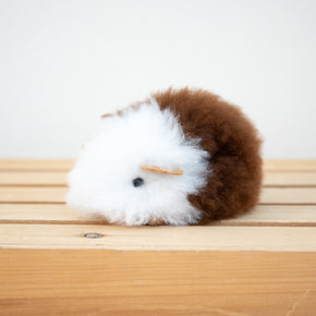 A plush toy resembling a guinea pig made from alpaca fur with white and brown coloring.