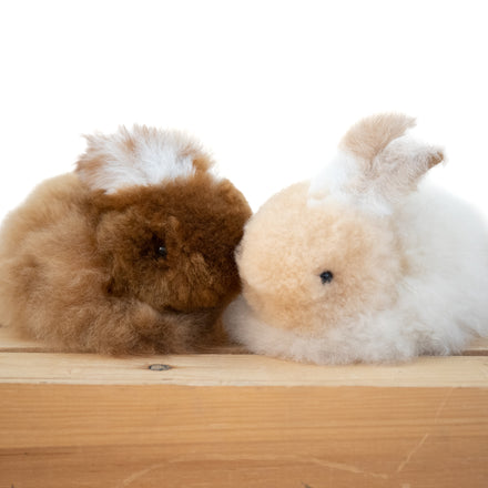 Two plush toy rabbits made from alpaca fur, one brown and one white, sitting next to each other.