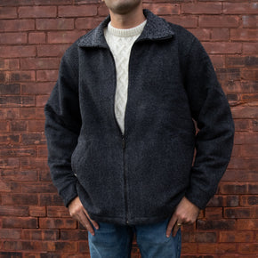 A man wearing a charcoal-colored alpaca and wool barn jacket with a faux sherpa lining, standing in front of a brick wall.