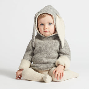 Baby wearing a gray and white knitted outfit with bunny ears on a light background