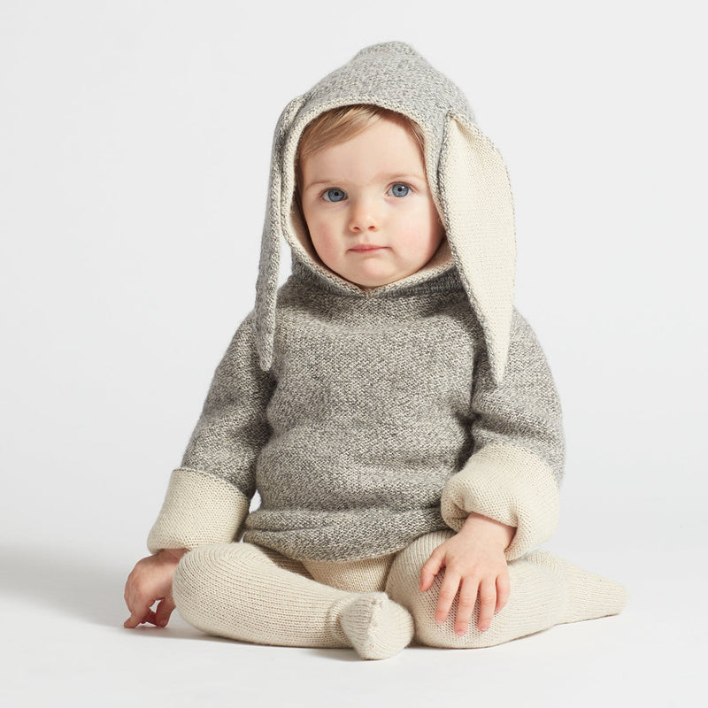 Baby wearing a gray and white knitted outfit with bunny ears on a light background