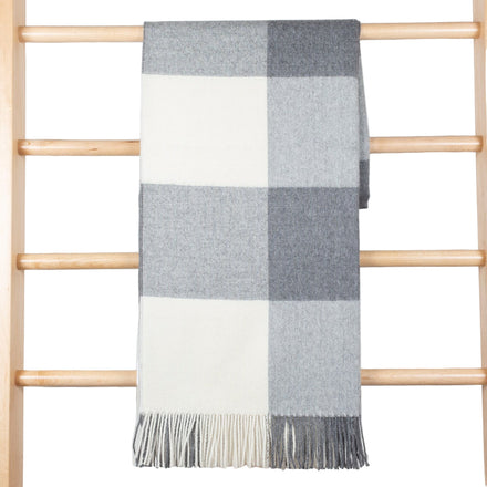 Plaid blanket with gray and white pattern draped over a wooden ladder against a light wooden panel background