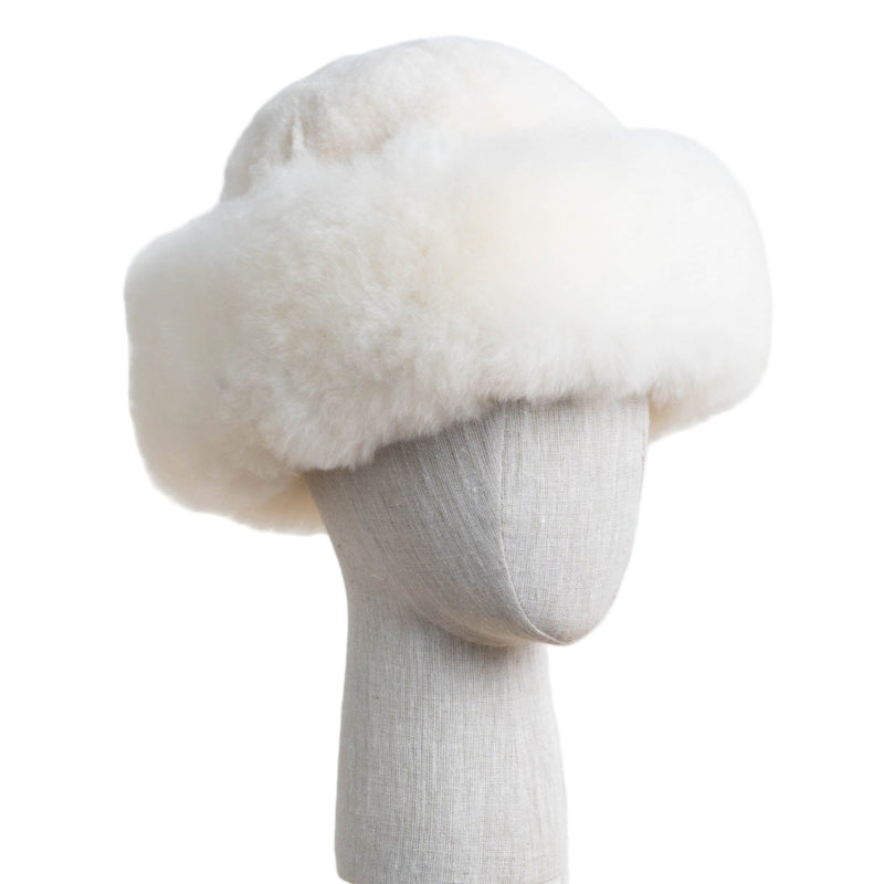 Premium Baby Alpaca Fur Hat. A natural white Premium Baby Alpaca Fur Hat on a mannequin head against a white paneled background.