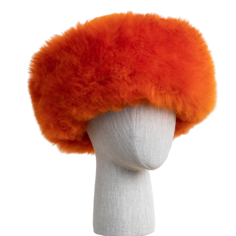Premium Baby Alpaca Fur Hat. An orange Premium Baby Alpaca Fur Hat on a mannequin head against a white paneled background.