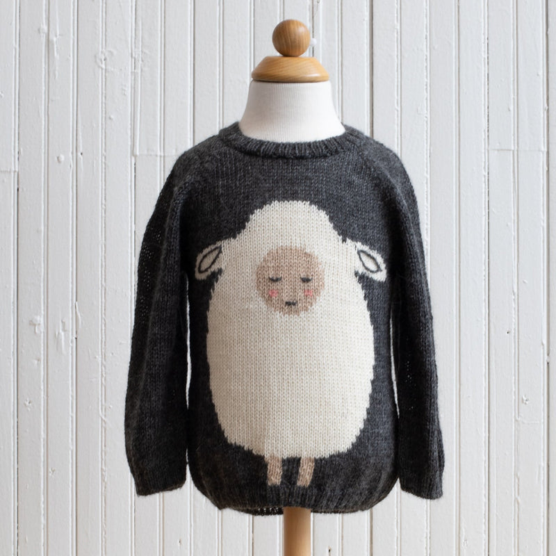 A gray baby alpaca sweater with a whimsical sheep design on the front, displayed on a wooden mannequin against a white wooden background.