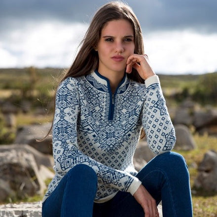 A woman sitting outdoors wearing a quarter zip sweater with geometric patterns in blue and white, paired with blue jeans.